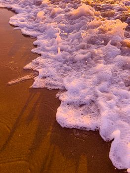 Vivid ocean waves create foamy patterns on the sandy shore during sunset.