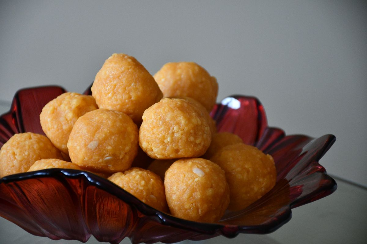 Close-up of sweet Indian laddu served in a decorative glass bowl against a gray background.