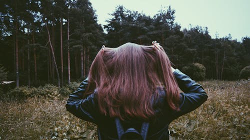 Woman in Black Leather Jacket Standing Before Green Leaved Trees