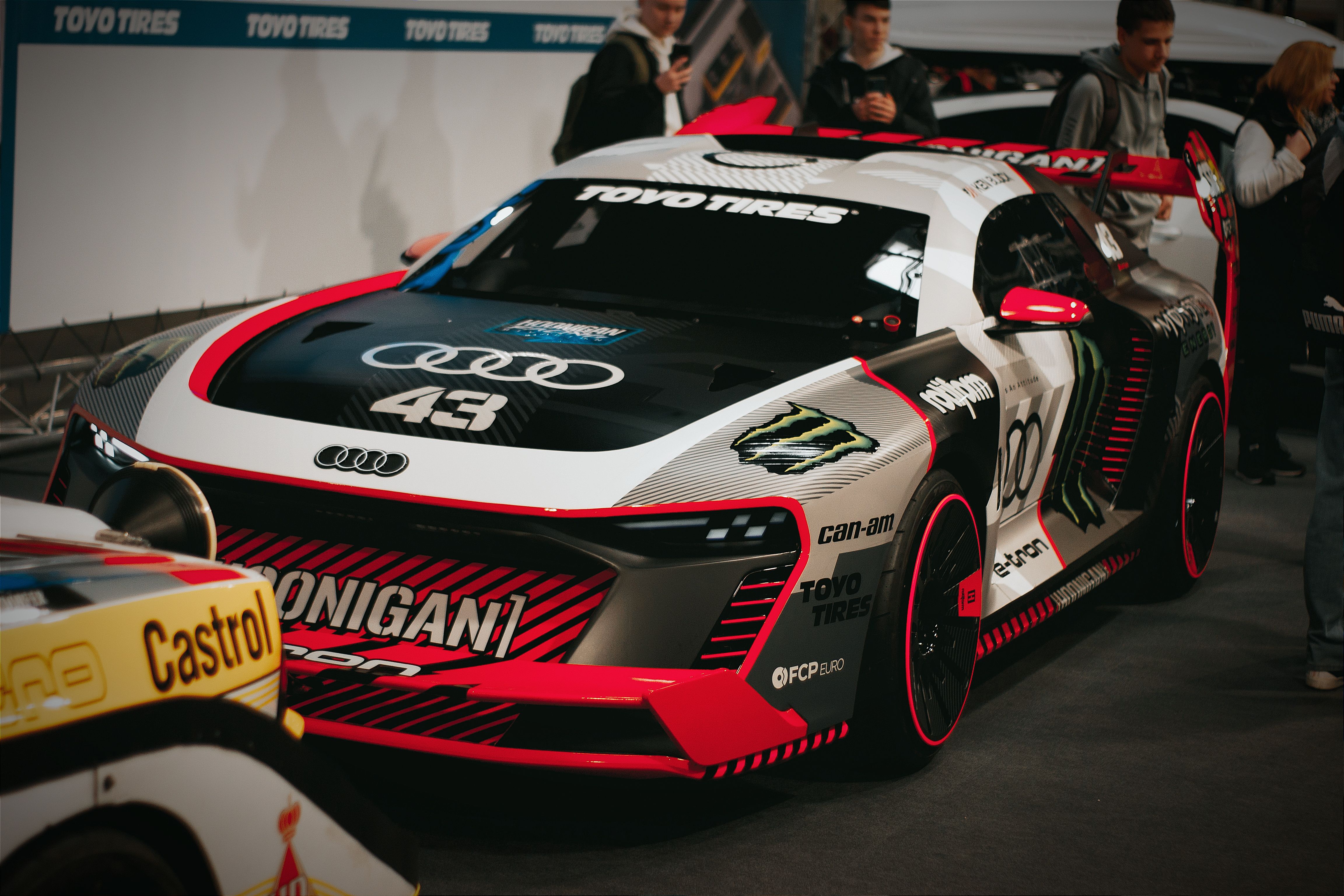 A sleek Audi R8 LMS race car with racing stripes parked indoors at a motorsport event.