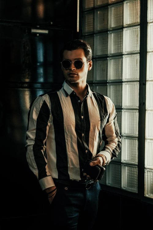 Free Fashionable man in sunglasses posing against a glass wall indoors. Stock Photo