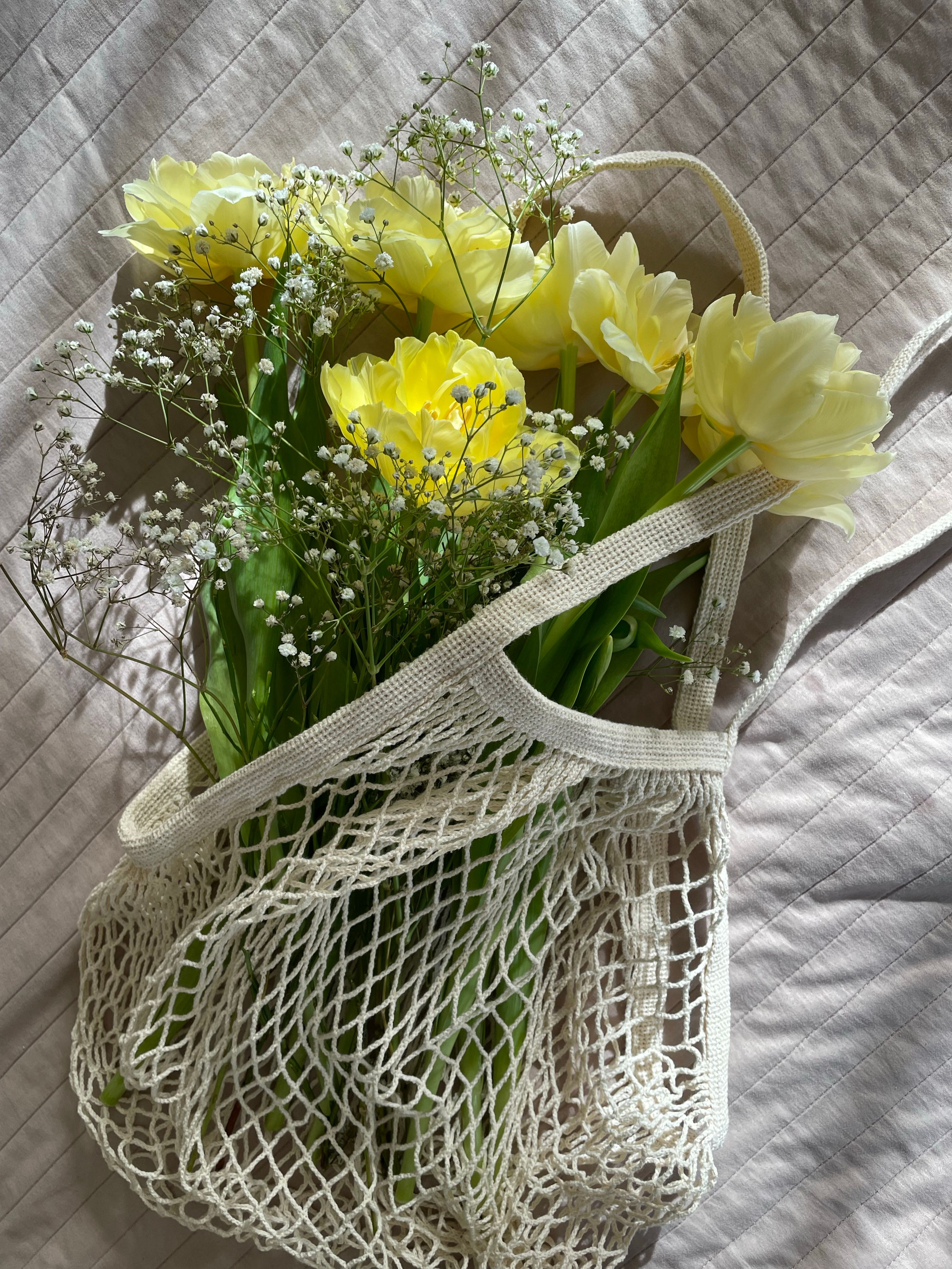 Aesthetic arrangement of yellow tulips with white flowers in a mesh bag on textured fabric.