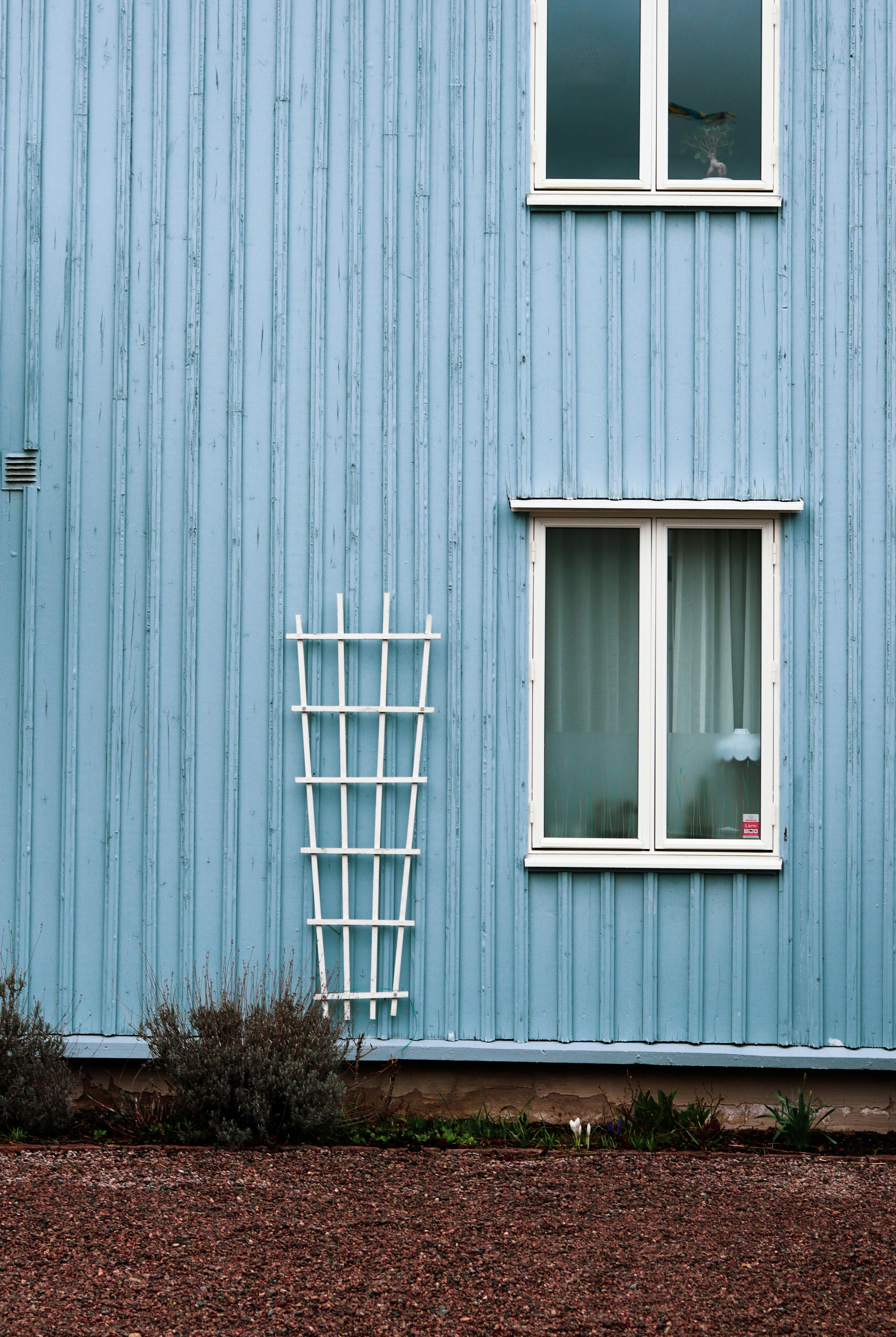 Blue wooden building with white-framed windows and a trellis, with brown gravel at the base.