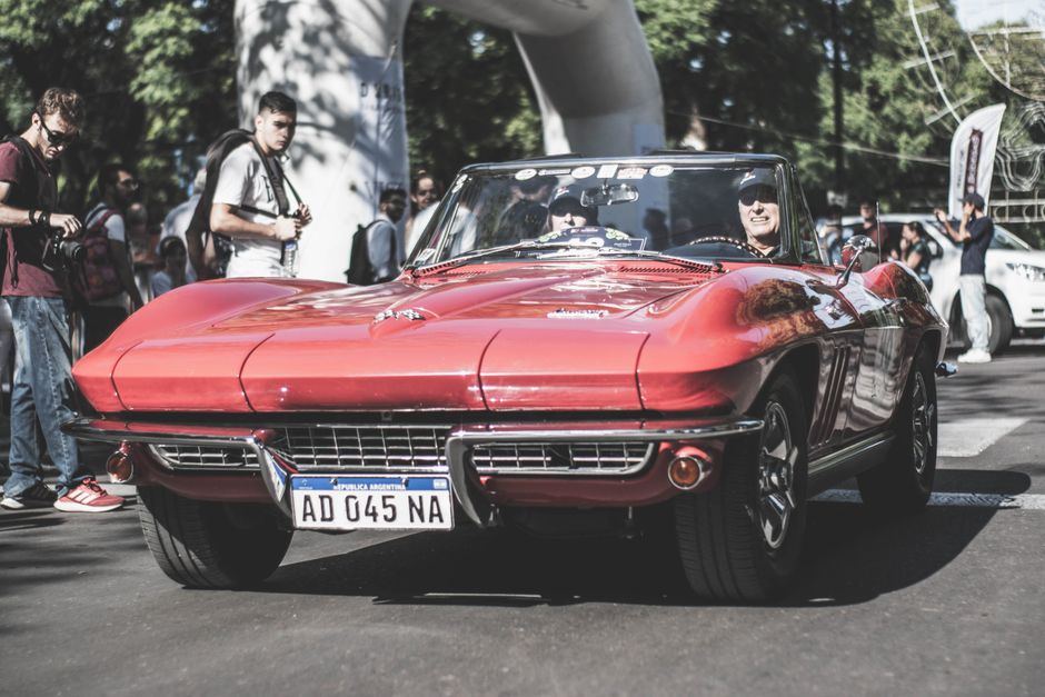Fotomural Un clásico Chevrolet Corvette convertible rojo circulando por las calles de la ciudad durante el día.