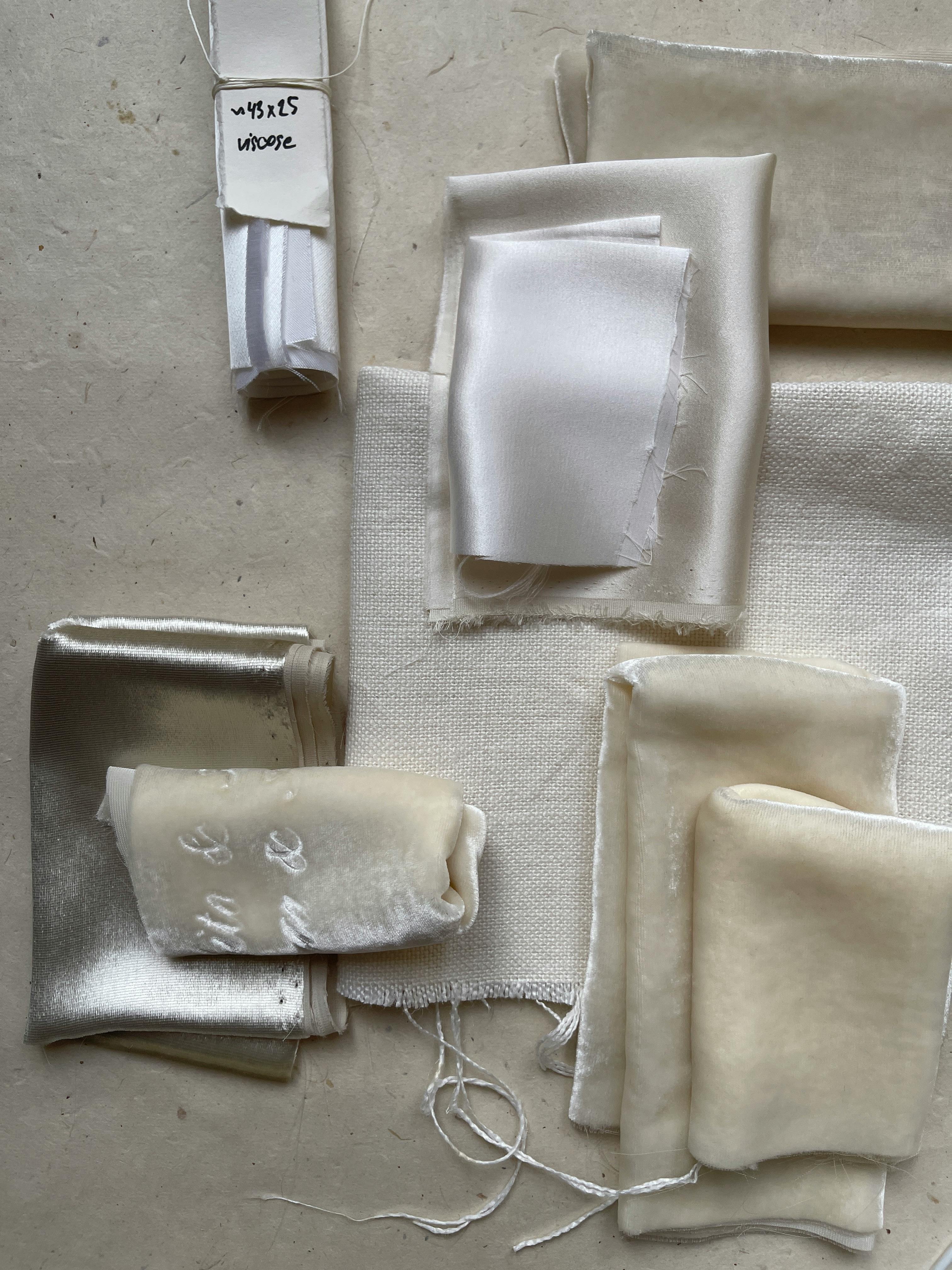 A collection of fabric swatches in neutral tones displayed on a beige surface.