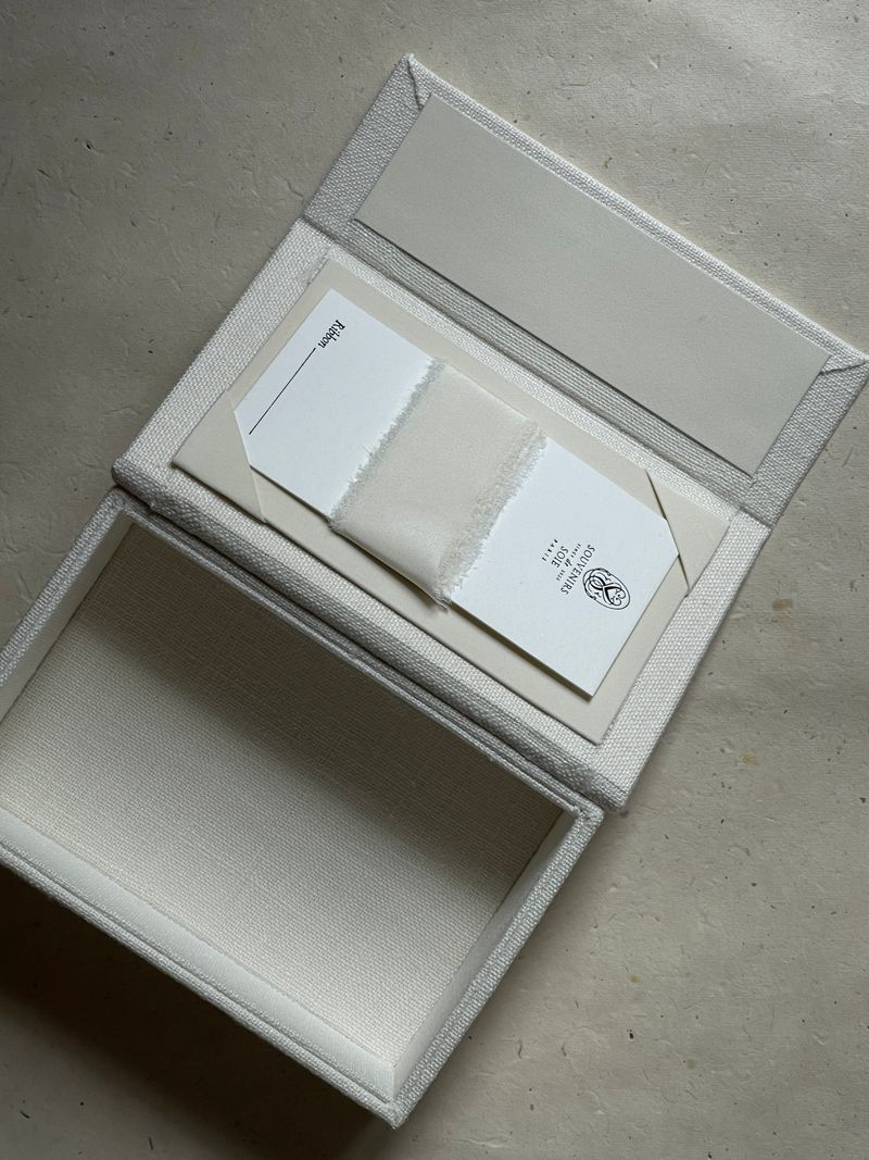 A sophisticated linen gift box displaying an elegant invitation card inside.