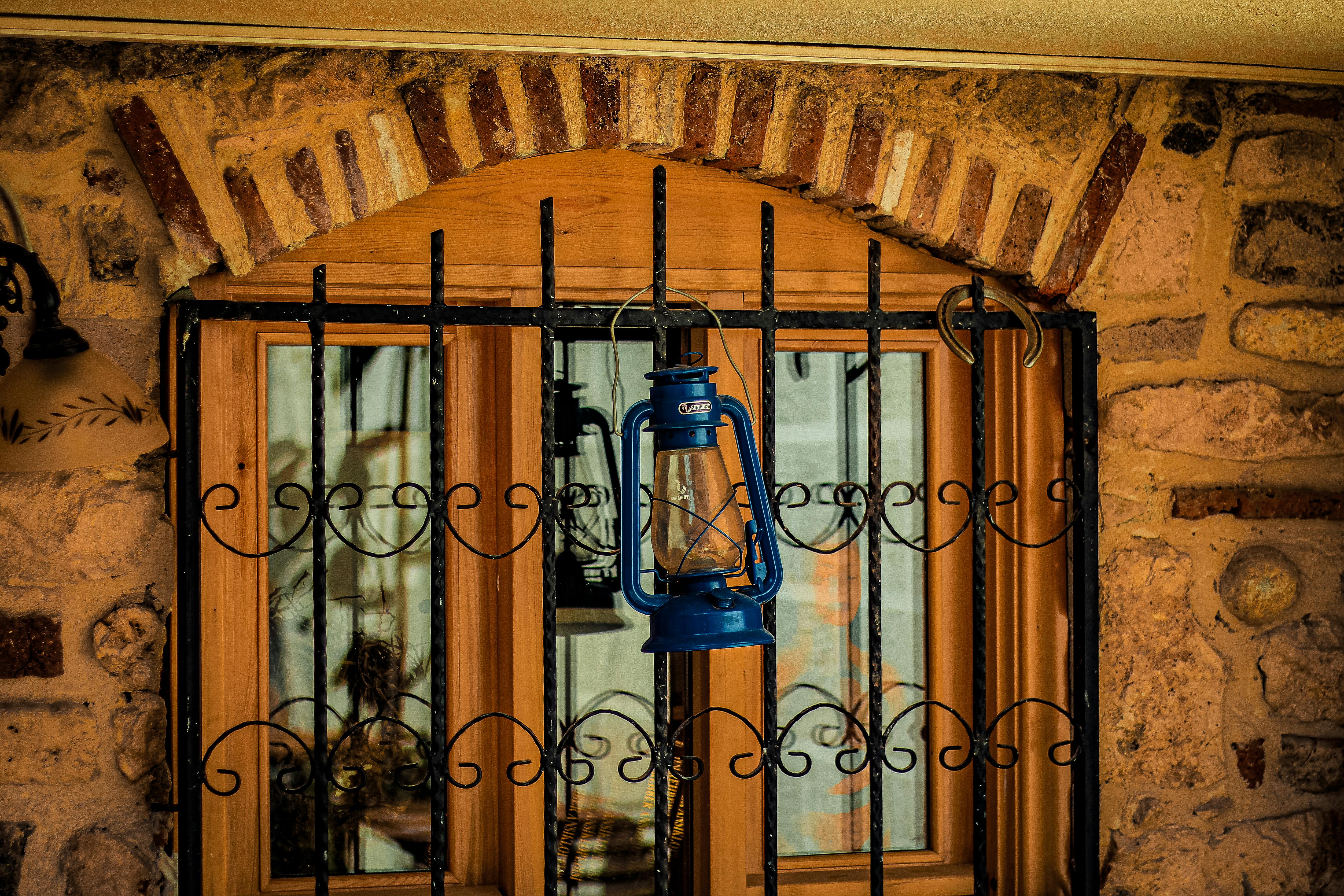 Free Vintage blue lantern hangs on a rustic stone wall window, framed by metalwork. Stock Photo