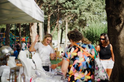 A lively scene of people shopping for jewelry at an outdoor market in a park during summer.