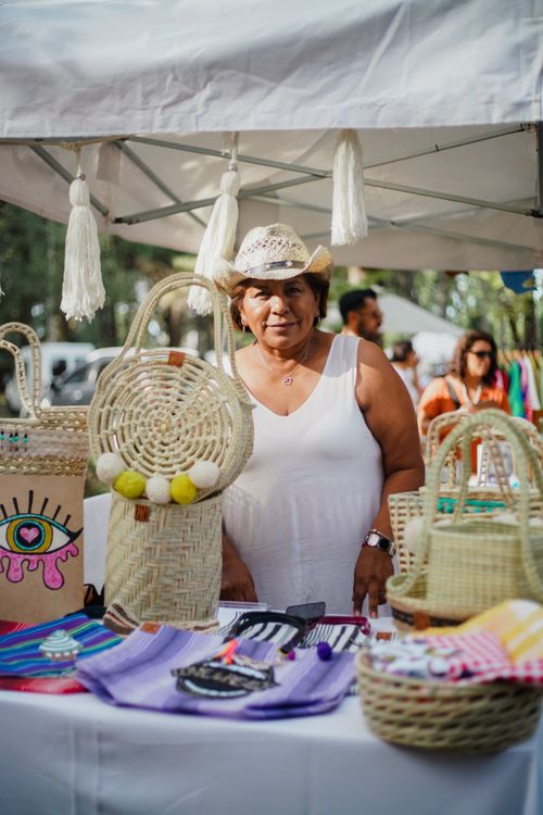 Free A woman vendor displays handmade crafts at an outdoor market, showcasing colorful, artisanal products. Stock Photo