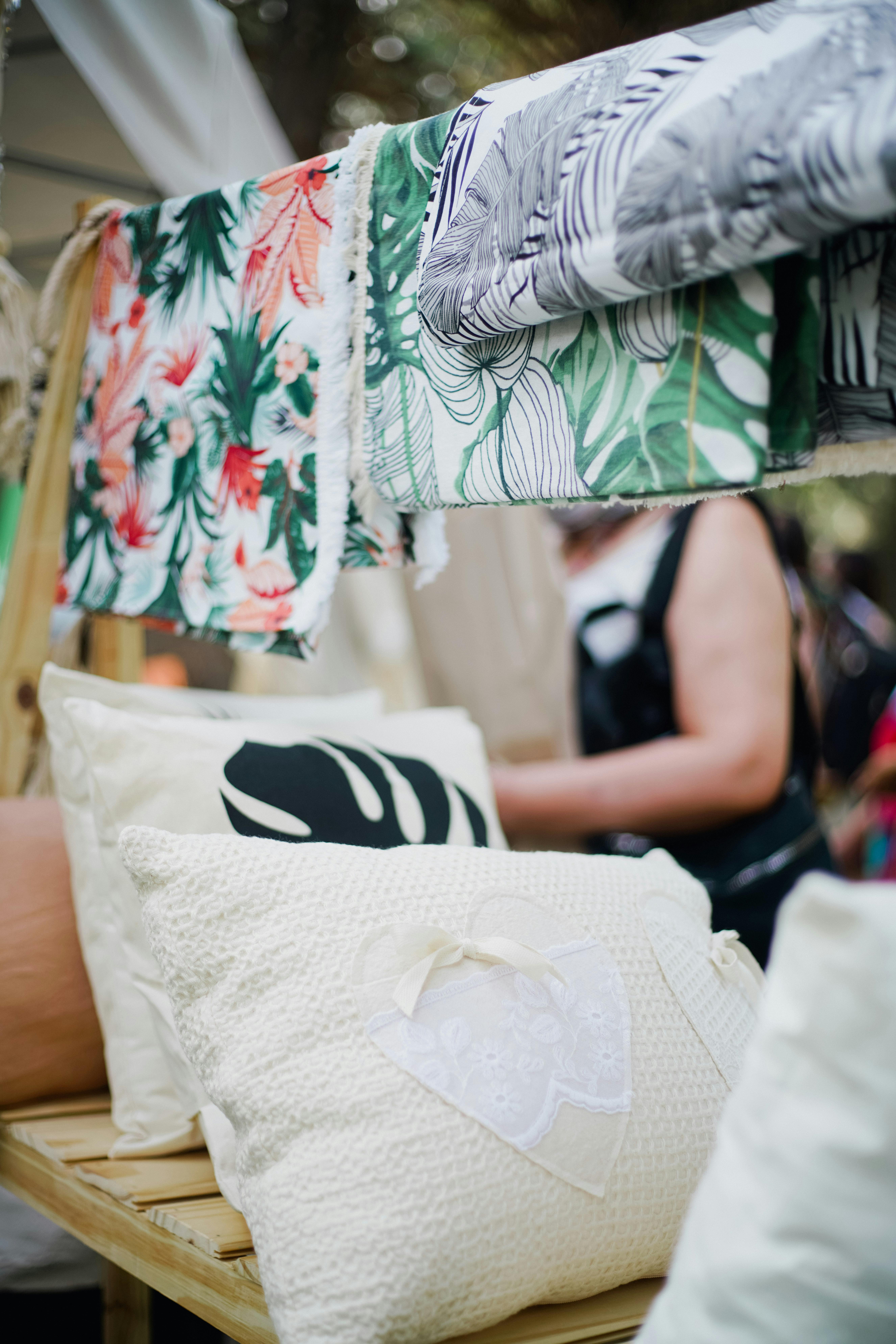 Vibrant display of patterned textiles and pillows at an outdoor market stall.