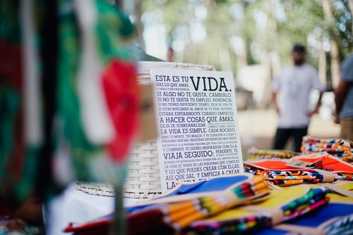 Free Vibrant market scene featuring colorful fabrics and an inspirational sign in Spanish. Stock Photo