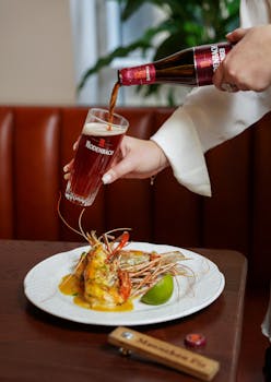 Close-up of beer being poured into a glass alongside a gourmet seafood dish in a restaurant setting.