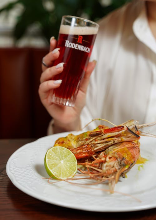 Woman Hand Holding Beer over Plate with Seafood
