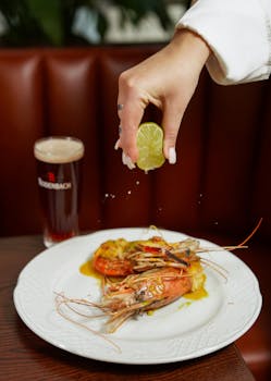 Close-up of lime being squeezed over prawns with a drink in the background.