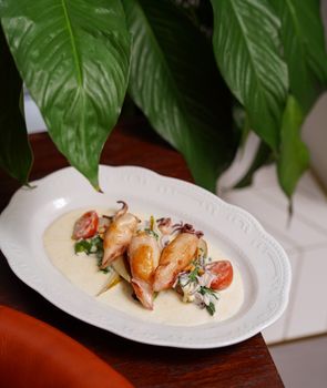 Close-up of a gourmet squid dish served with creamy sauce, tomatoes, and greens on a white plate.