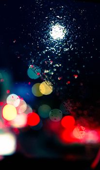 Raindrops on a window create a bokeh effect with vibrant city lights at night, offering a dreamy urban scene.
