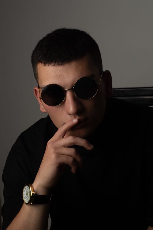 Free Young man in sunglasses and black t-shirt posing confidently in a studio setting. Stock Photo
