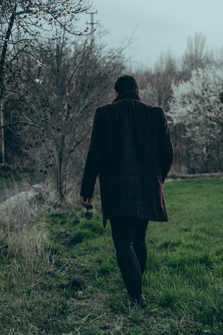 Back View Of A Man In A Black Coat Walking In The Park 