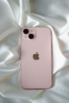 Pink smartphone with dual cameras placed on luxurious white satin fabric.