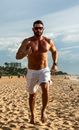 Muscular man jogging on João Pessoa's sandy beach under summer sun.