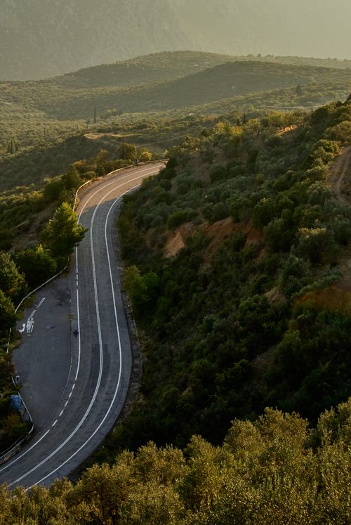 Free A winding mountain road surrounded by lush greenery under a serene, golden sky. Stock Photo