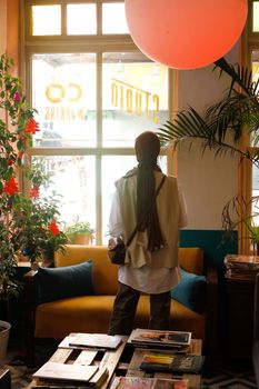 Woman in hijab standing by window in a stylish indoor lounge space.