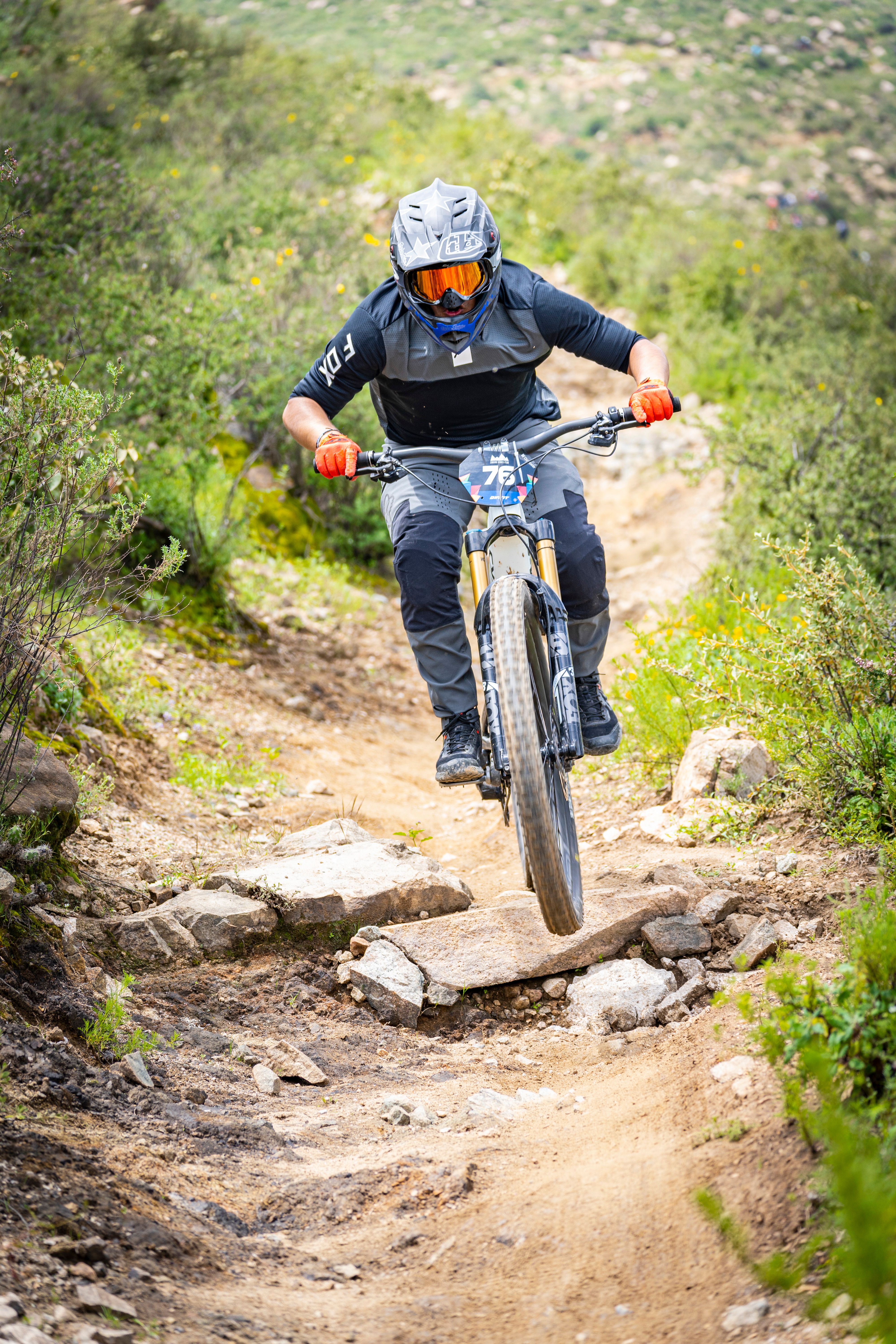 A mountain biker wearing protective gear jumps on a rocky outdoor trail.