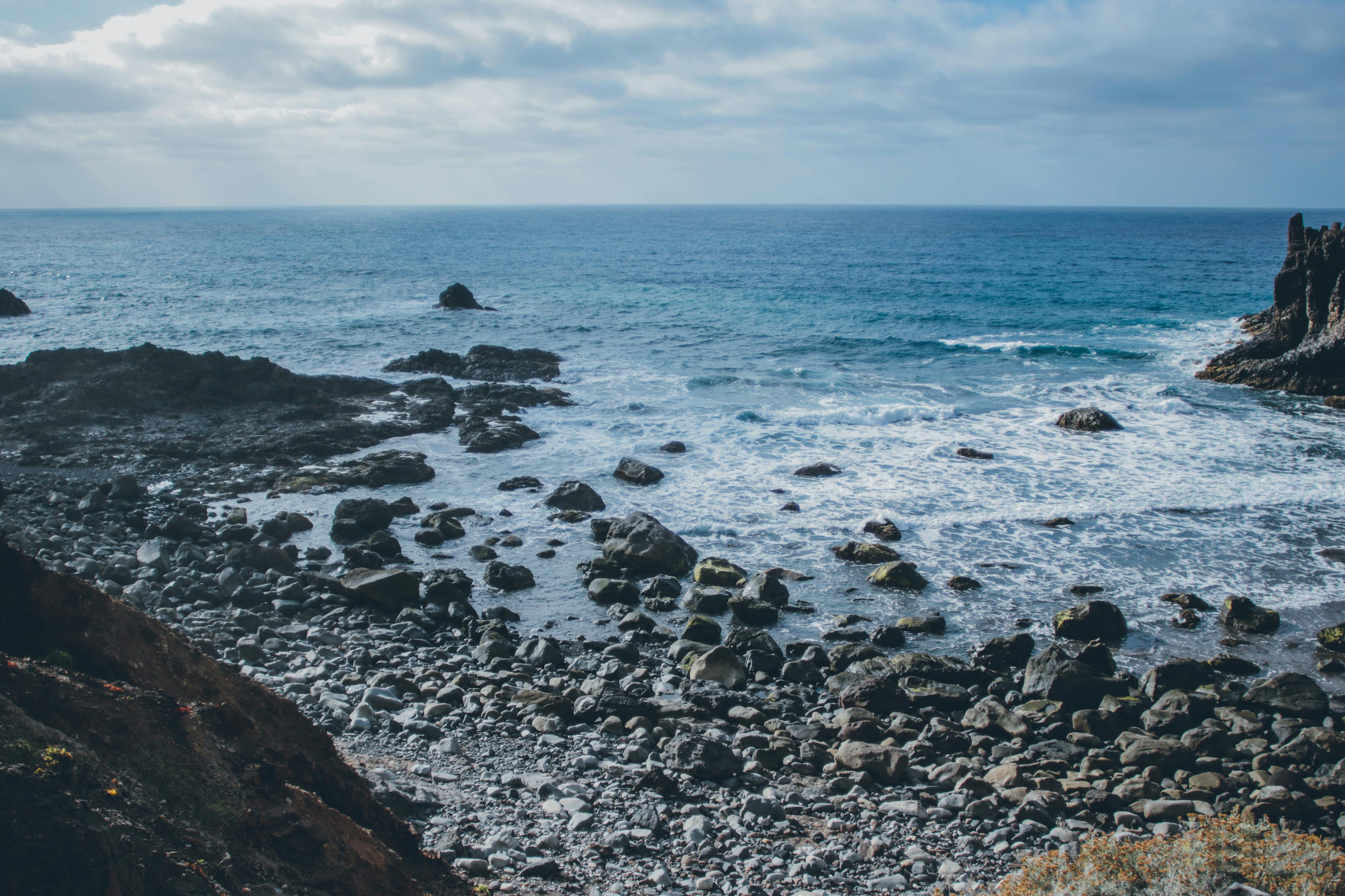 岩石海滩上，海浪在蓝天下拍岸，非常适合营造宁静的海景视觉效果