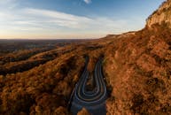 从空中俯瞰，蜿蜒的道路穿过充满活力的秋日森林与山脉，景色壮丽