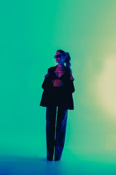 Fashionable woman in a stylish outfit poses confidently in a green-lit studio.
