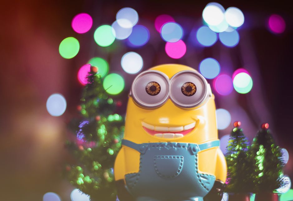 A cheerful minion toy among colorful bokeh lights and small Christmas trees.