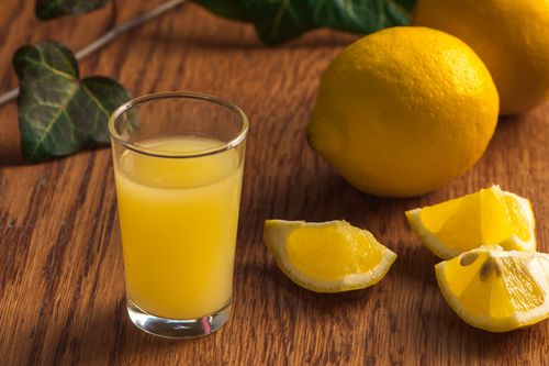 Free Freshly squeezed lemon juice in a glass with sliced lemons on wooden surface. Stock Photo