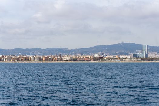 Stunning panoramic view of Barcelona coastline with urban skyline and distant hills under a cloudy sky.