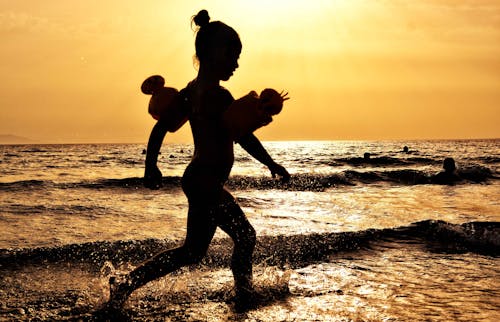 Gratis Siluet Gadis Berlari Di Tepi Laut Selama Golden Hour Foto Stok