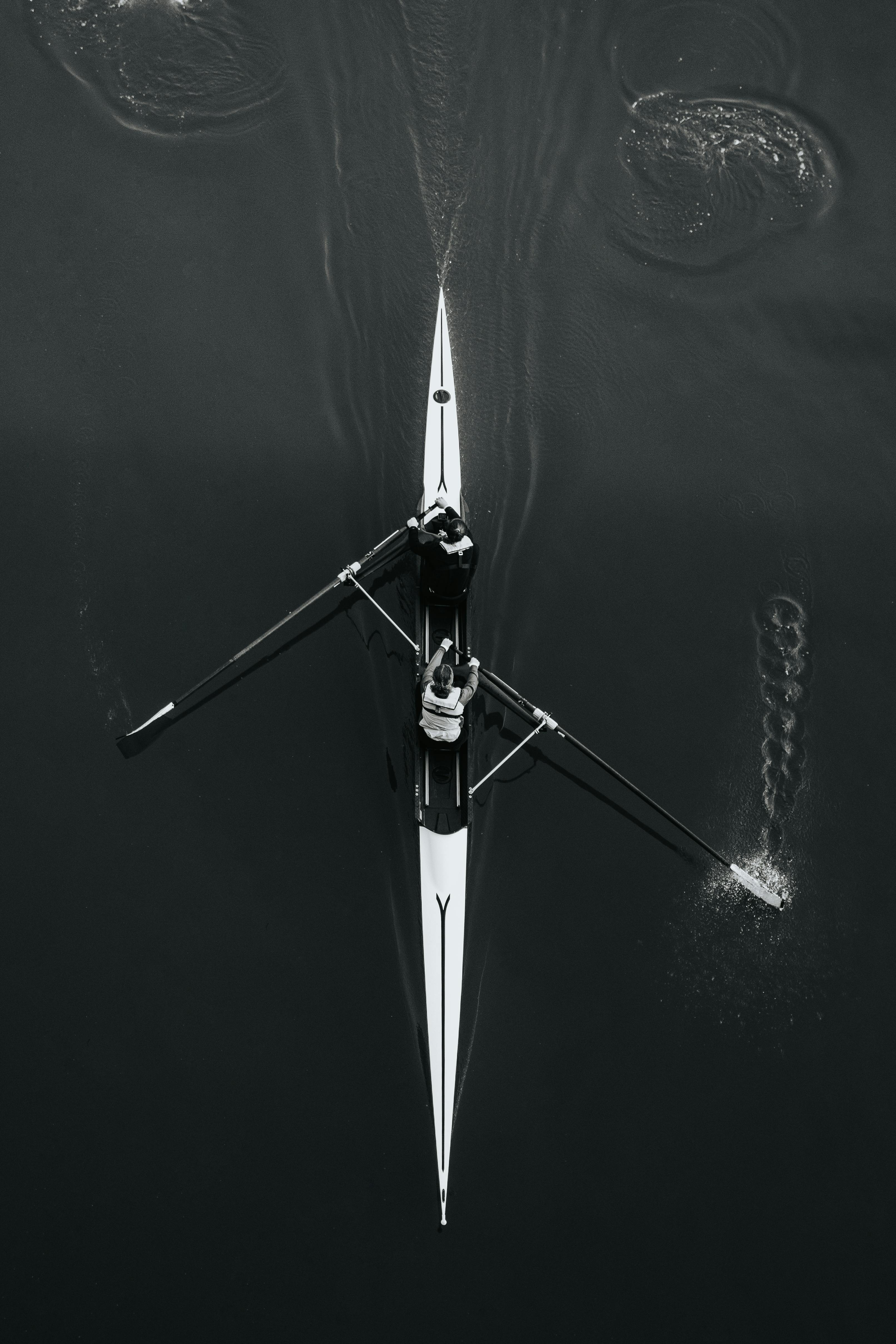 Overhead shot of two rowers paddling in sync on calm waters, showcasing teamwork.