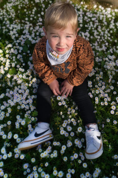 Blonde Boy Sitting on Meadow with Flowers