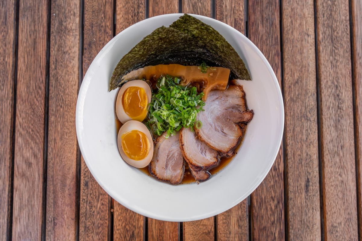 A bowl of tonkotsu ramen with chashu pork, soft-boiled egg, scallions, and seaweed on a wooden table