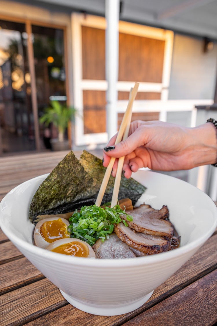 A Person Holding Chopsticks In A Bowl Of Food