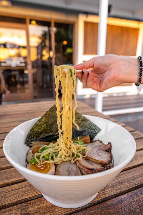 A person holding a fork over a bowl of ramen