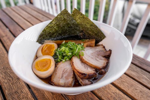 A bowl of ramen with pork, eggs and greens