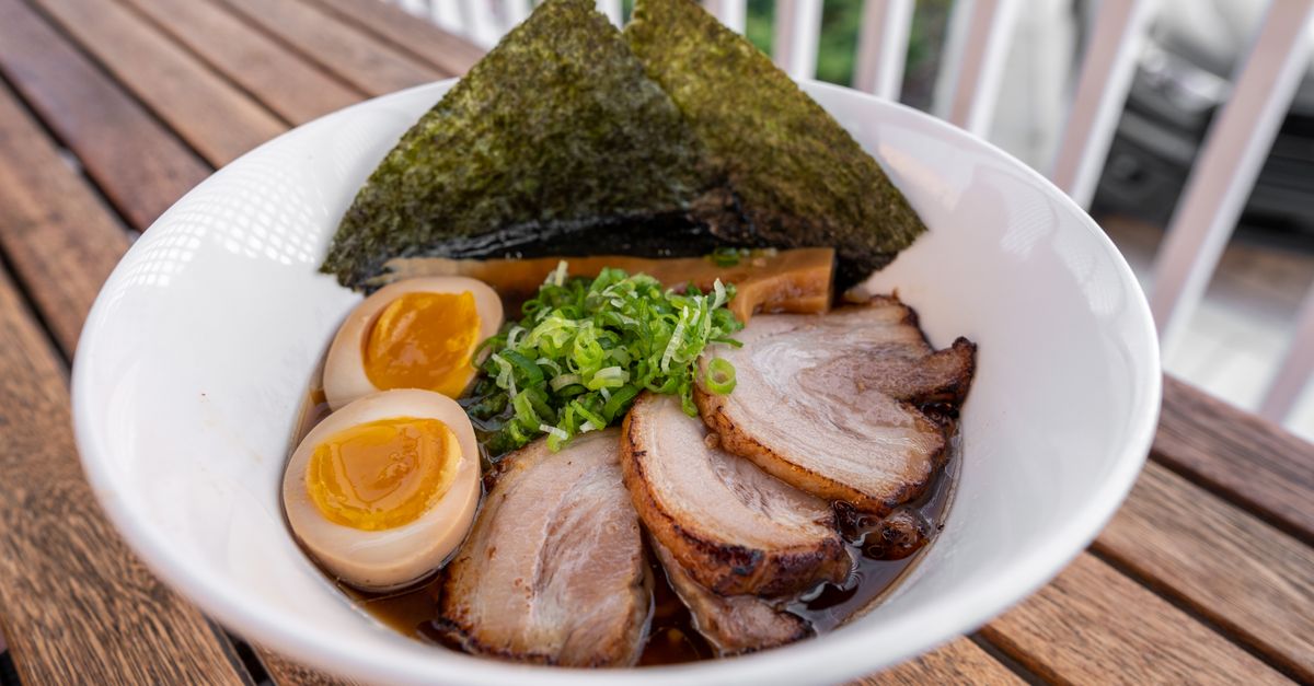 Sliced chashu pork over a ramen bowl Bowl of ramen topped with sliced chashu pork, soft egg, and green onions