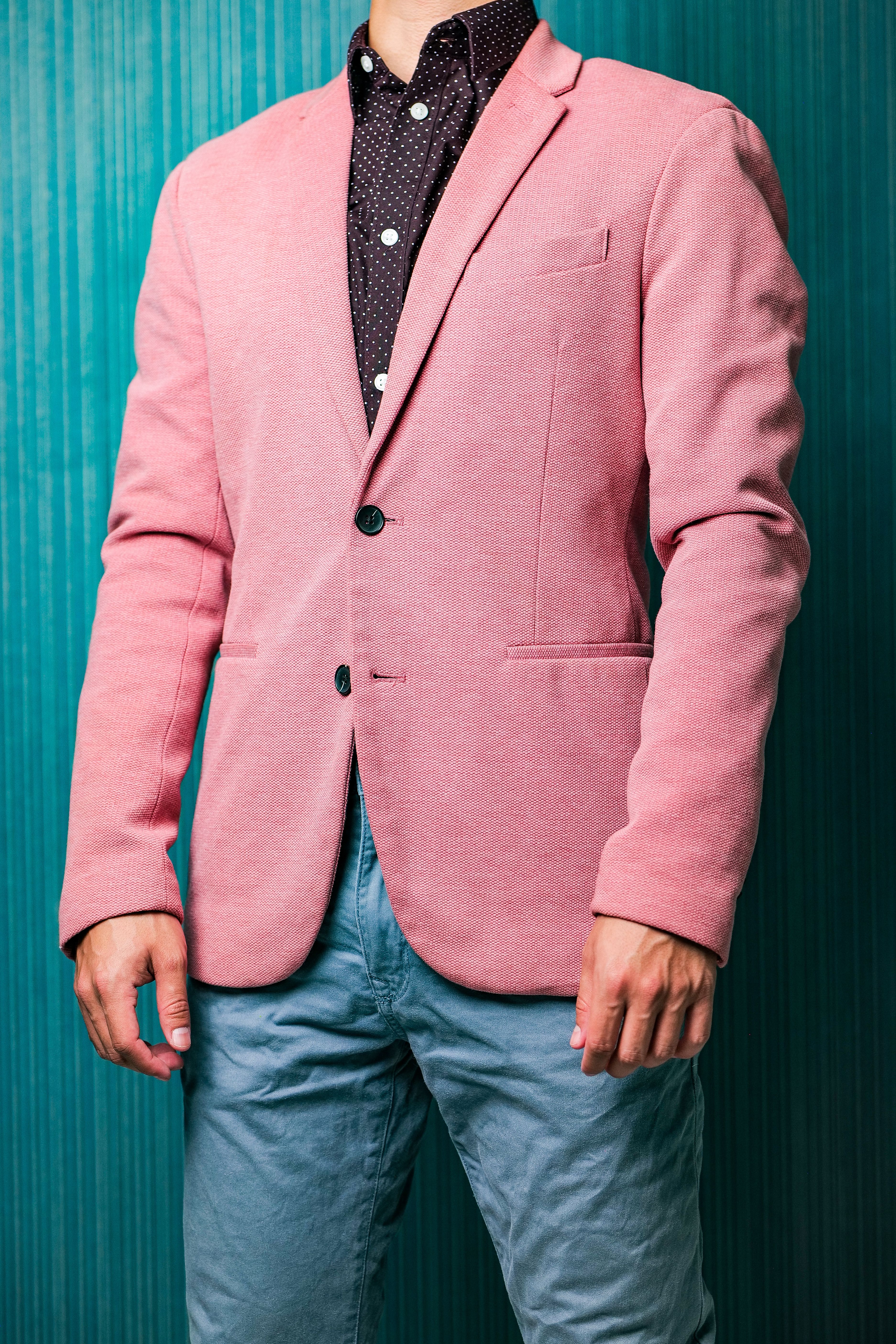 A man showcases a fashionable pink blazer paired with casual jeans in a studio setting.