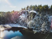 明亮的日光下，白雪覆盖的悬崖、树木和平静的湖泊构成了一幅宁静的冬季景象