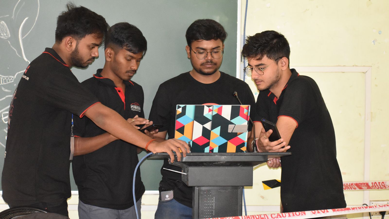 Indian students collaborating on a laptop beside a classroom board