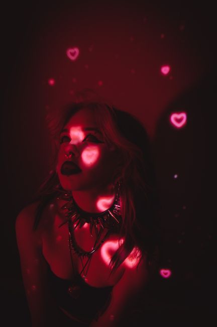 Artistic photo of a woman with heart-shaped light projections on her face, creating a dramatic effect.
