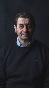 Studio portrait of a middle-aged man smiling in a black sweater against a dark background.