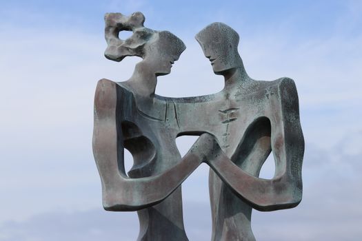 Modern abstract sculpture depicting a couple in an urban setting against a clear blue sky.