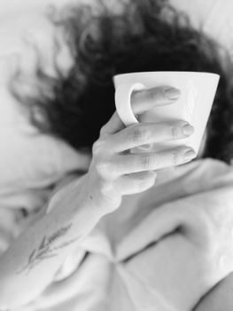 A person enjoying a peaceful morning with coffee in bed, shot in black and white.