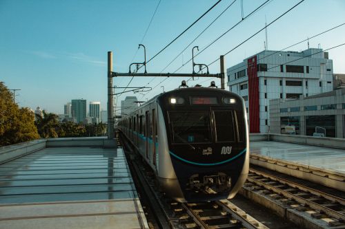 Free View of a modern metro train on an elevated track in Jakarta, Indonesia, with city skyline in the background. Stock Photo