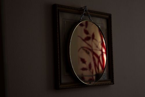 Free An oval mirror with chain hanging reflects abstract art, creating a moody atmosphere indoors. Stock Photo